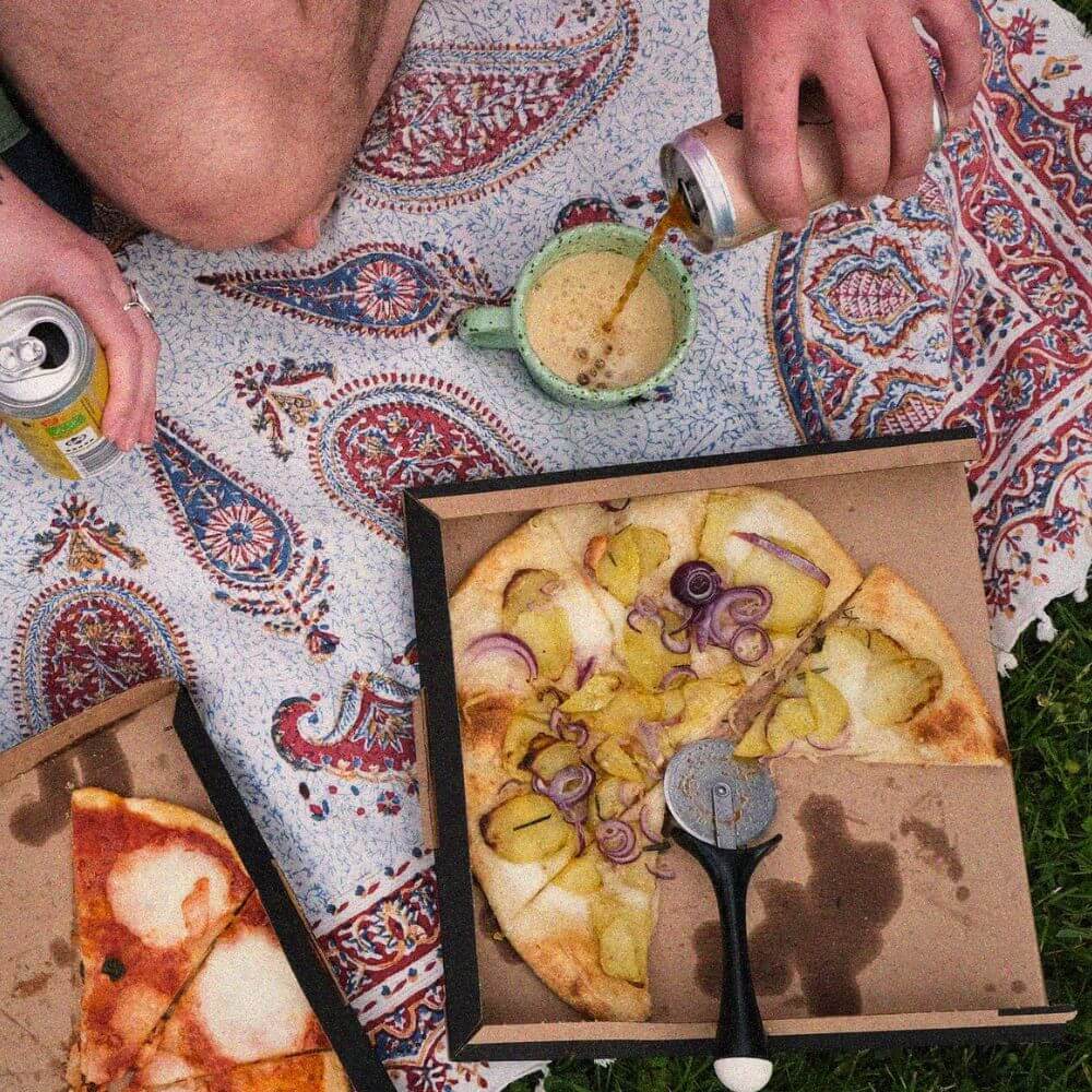Picnic blanket with two pizzas and two craft sodas.