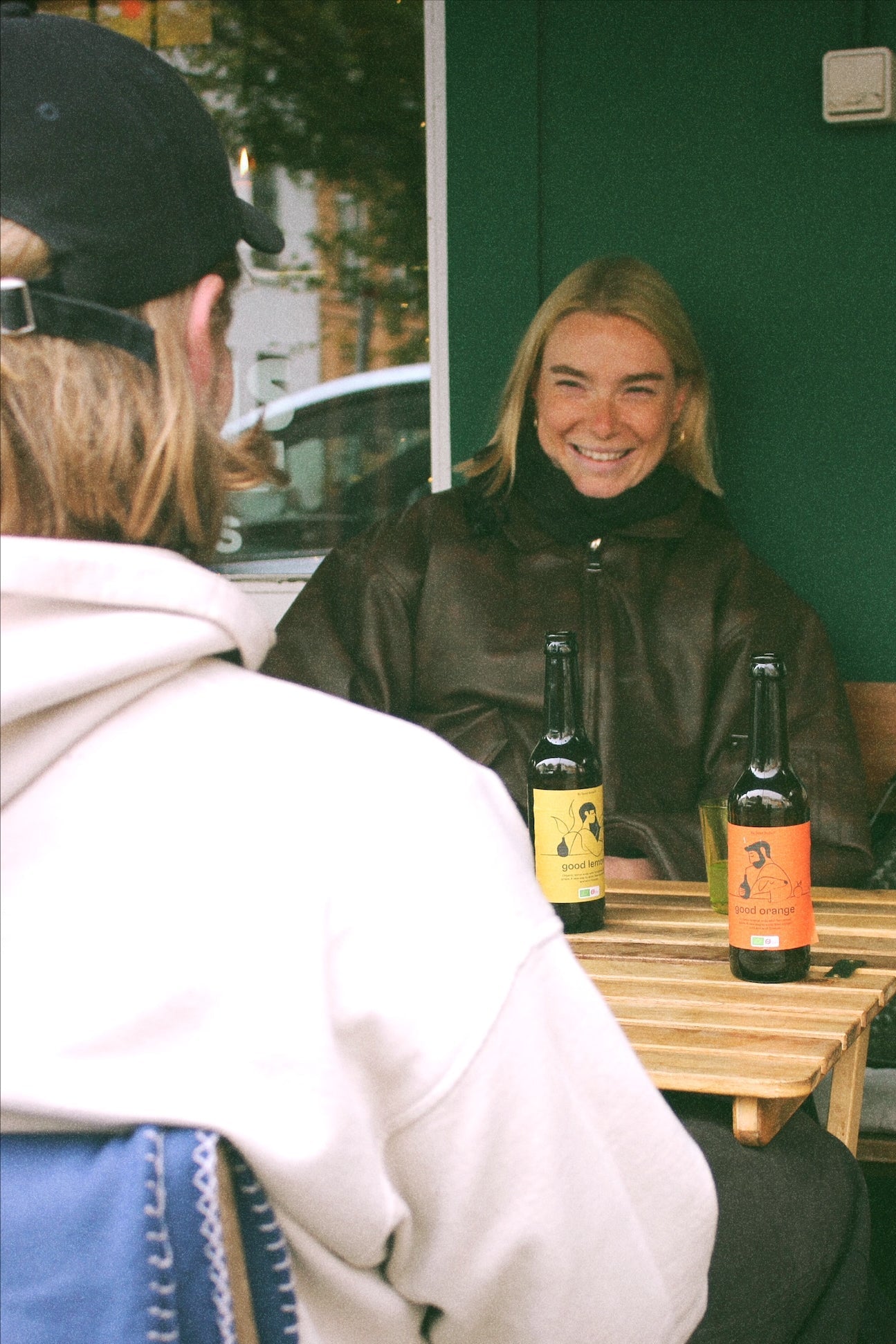 Person sitting at a table with two bottles of organic and fermentet good soda with in a casual setting. The bottles are good lemon® and good orange®