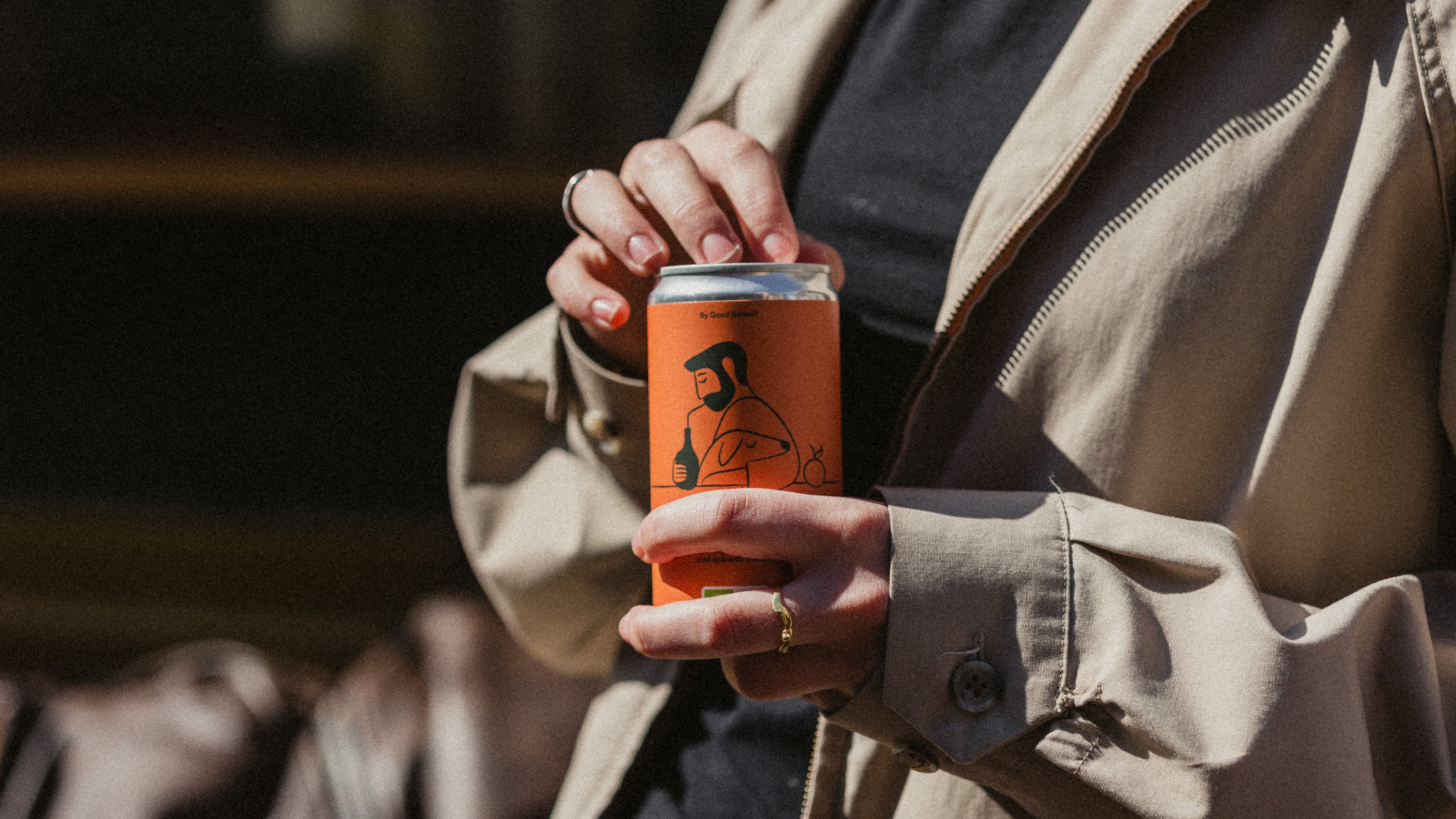 woman holding an organic and fermentet good orange can with orange label, wearing a beige coat.