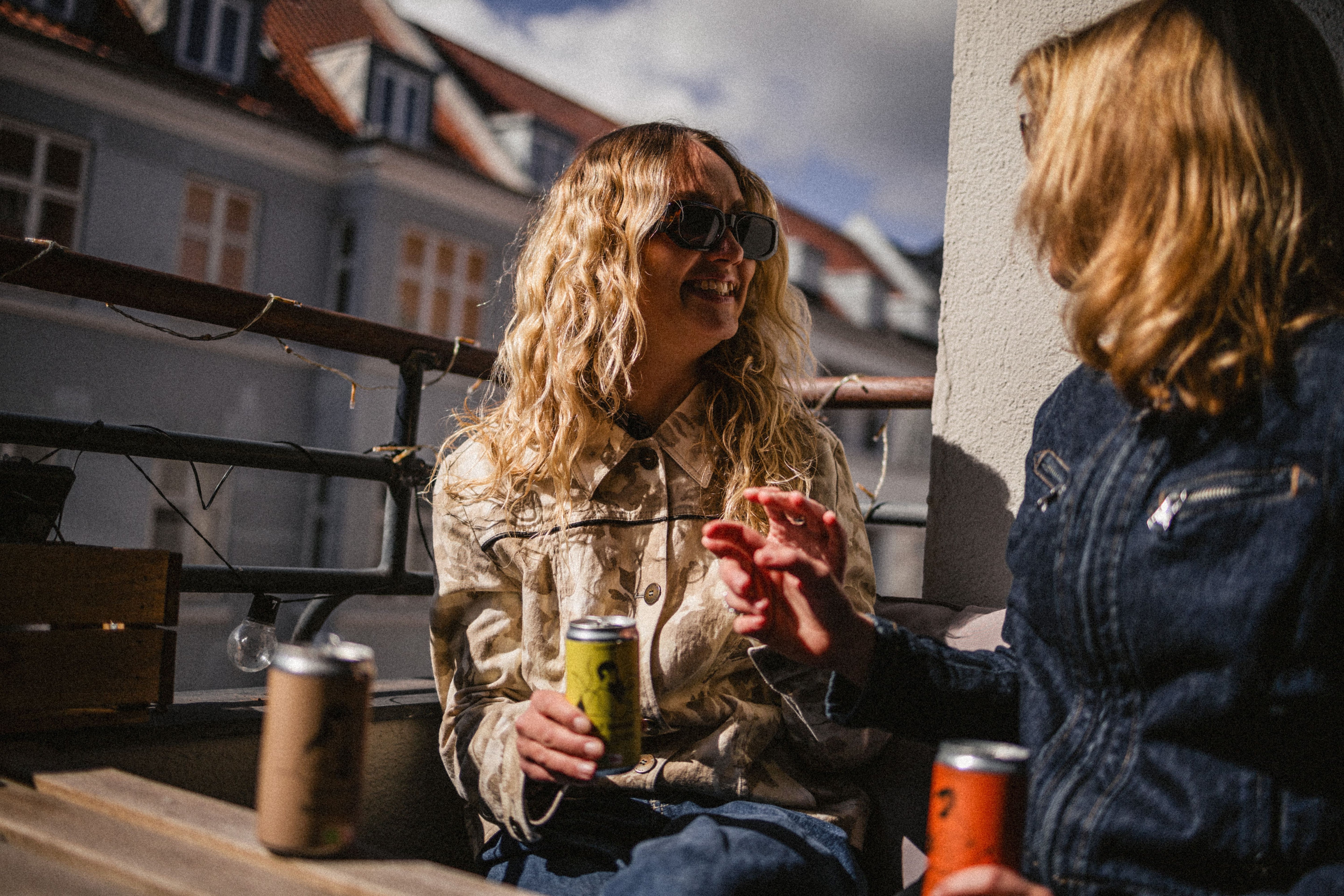 Two people sitting on a balcony, one holding a good lemon®, another holding a good orange® with a building in the background.
